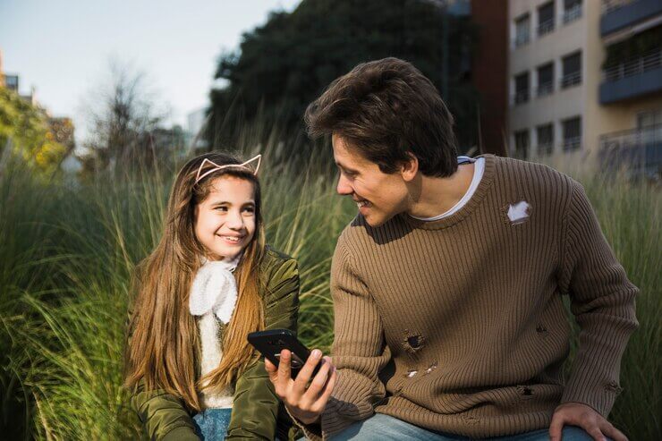 Role of Communication: happy father and daughter looking at each other holding mobile phone in hand