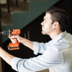 Locksmith Pasadena MD Servleader, an attractive handyman using a power drill to fix a door knob in a house
