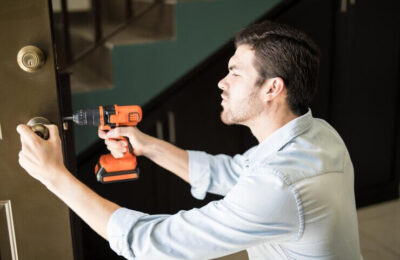 Locksmith Pasadena MD Servleader, an attractive handyman using a power drill to fix a door knob in a house