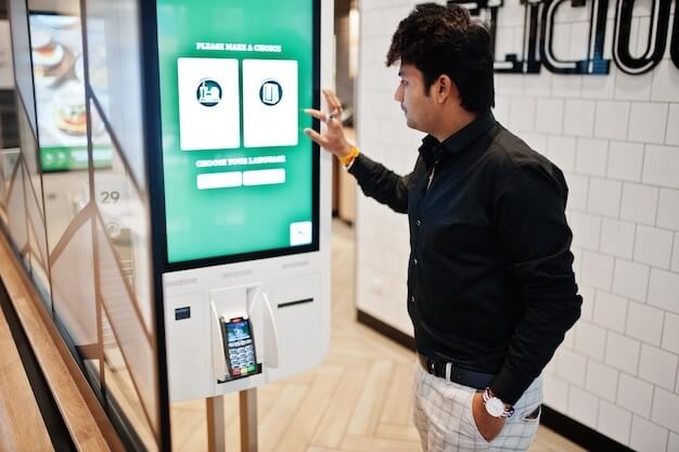 jcp kiosk: indian man customer at store place orders and pay through self pay floor kiosk for fast food payment terminal make a choise of language on screen