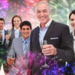 Smiling inernational business team holding glasses of Chamoagne against colourful fireworks exploding on black background