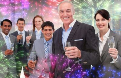 Smiling inernational business team holding glasses of Chamoagne against colourful fireworks exploding on black background