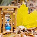 Sand clock and a large yellow maple leaf in the autumn forest