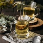 High angle hand pouring tea in glass with teapot