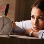 Displeased businesswoman hitting alarm clock with hammer in the office