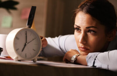 Displeased businesswoman hitting alarm clock with hammer in the office