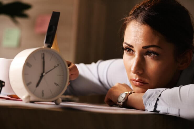 Displeased businesswoman hitting alarm clock with hammer in the office