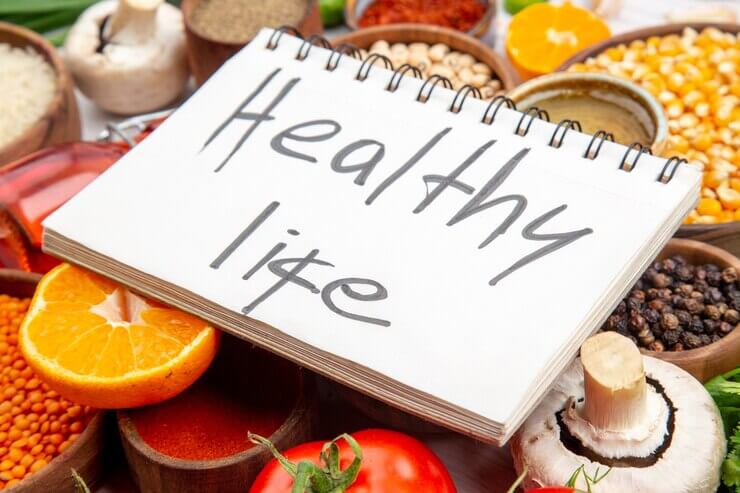 Side view of a healthy life inscription on spiral notebook on fresh vegetables lemon corn kernels lemon fallen oil bottle honey on white background