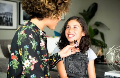 Woman In Black Floral Long Sleeve Shirt Holding A Bottle Of Essential Oil, talking with a young girl