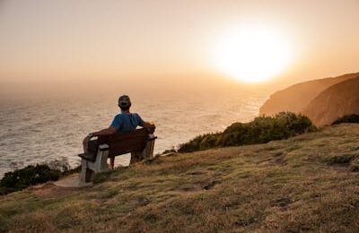 A Person Sitting on a Wooden Bench Looking at the Sunset