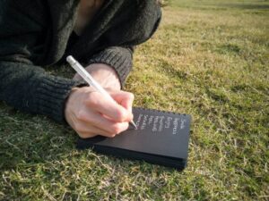 Person Writing on Book Lying Down on the Ground