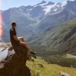 A Person Sitting on a Rock Formation Overlooking a Snow Capped Mountain