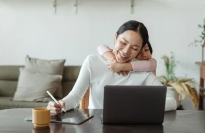Happy mother working from home and little daughter hugging mom