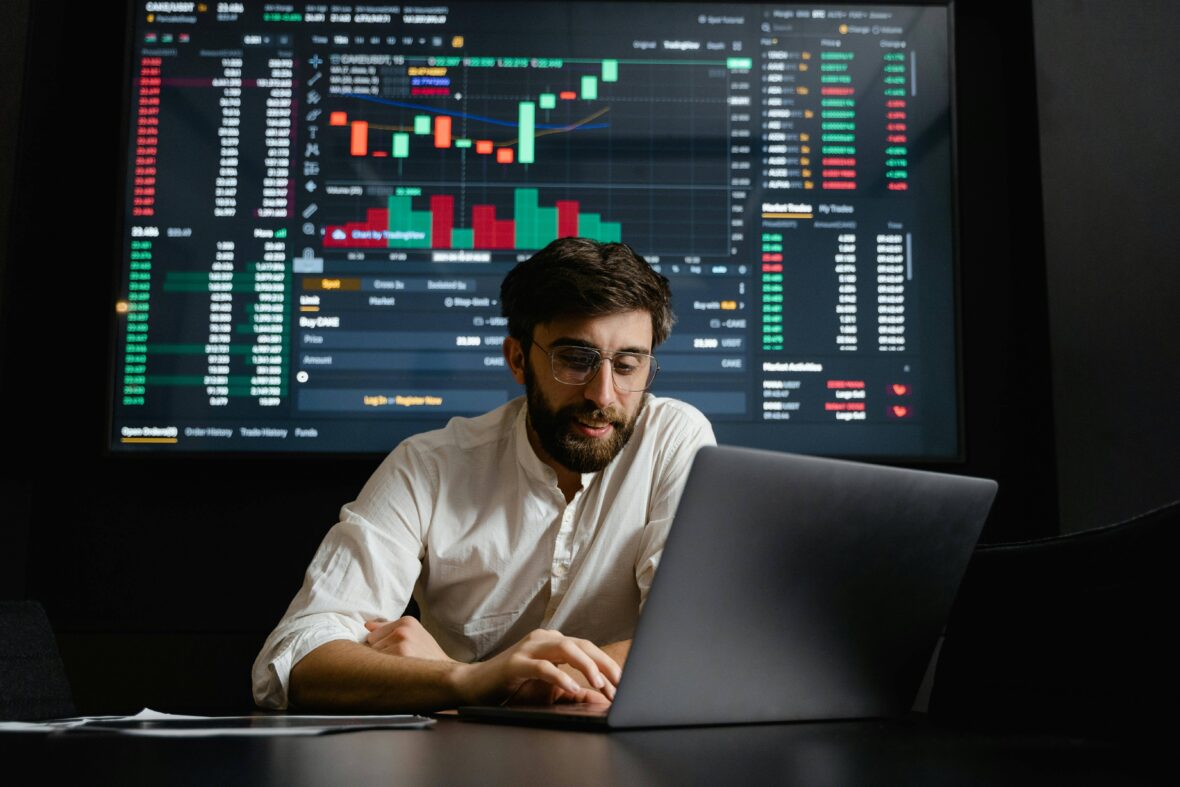 A man is working on laptop. In background stock exchange screen is showing