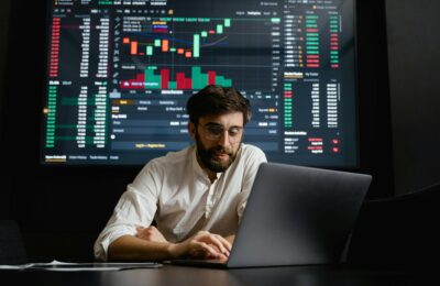 A man is working on laptop. In background stock exchange screen is showing